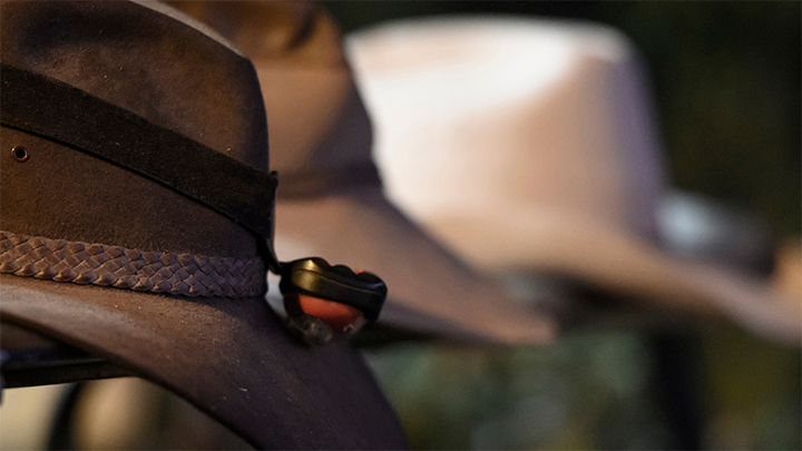 Close-up of three brown outback hats with braided bands displayed in soft focus.