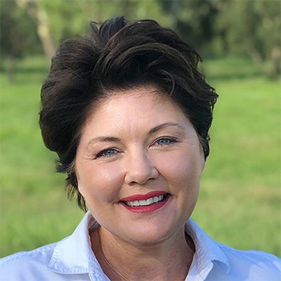 Headshot of RASF Board Member Jocellin Jansson smiling outdoors, wearing a white shirt with a green leafy background.
