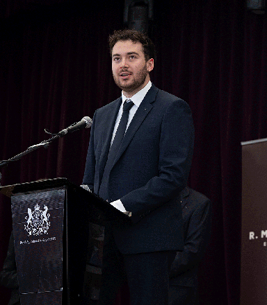 JB Fairfax Award 2025 winner Nick Newling in a dark suit, speaking at a podium in front of RAS Foundation banners.