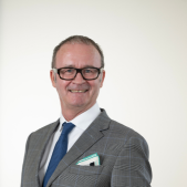 Headshot of Arts and Craft Committee Chair James Dorahy, smiling and wearing glasses, a grey suit, white shirt, and blue tie.