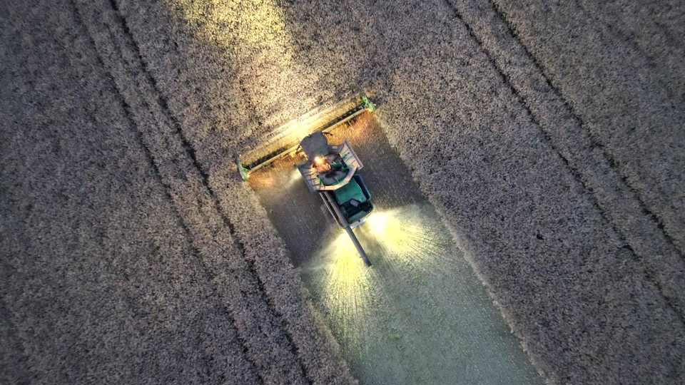 Aerial view of a combine harvester working through a crop field at night with bright lights.