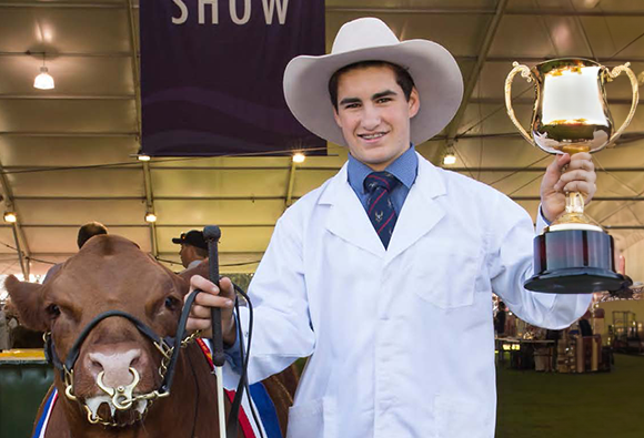 A young exhibitor in a white coat holding a trophy beside a prize-winning bull.
