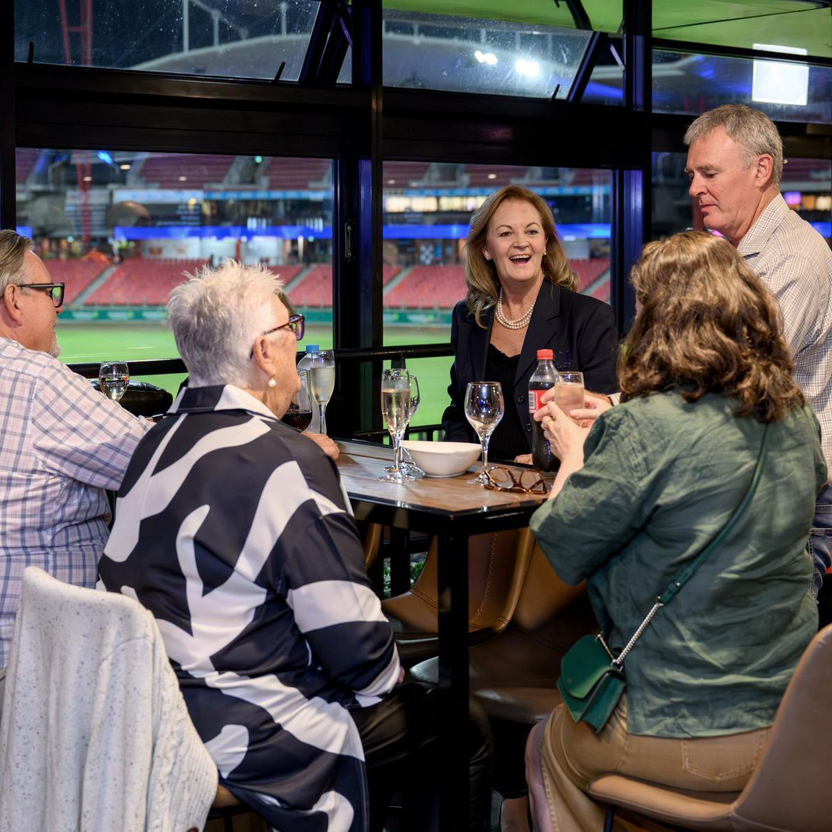 Group of adults enjoying drinks and conversation inside a venue overlooking ENGIE Stadium.