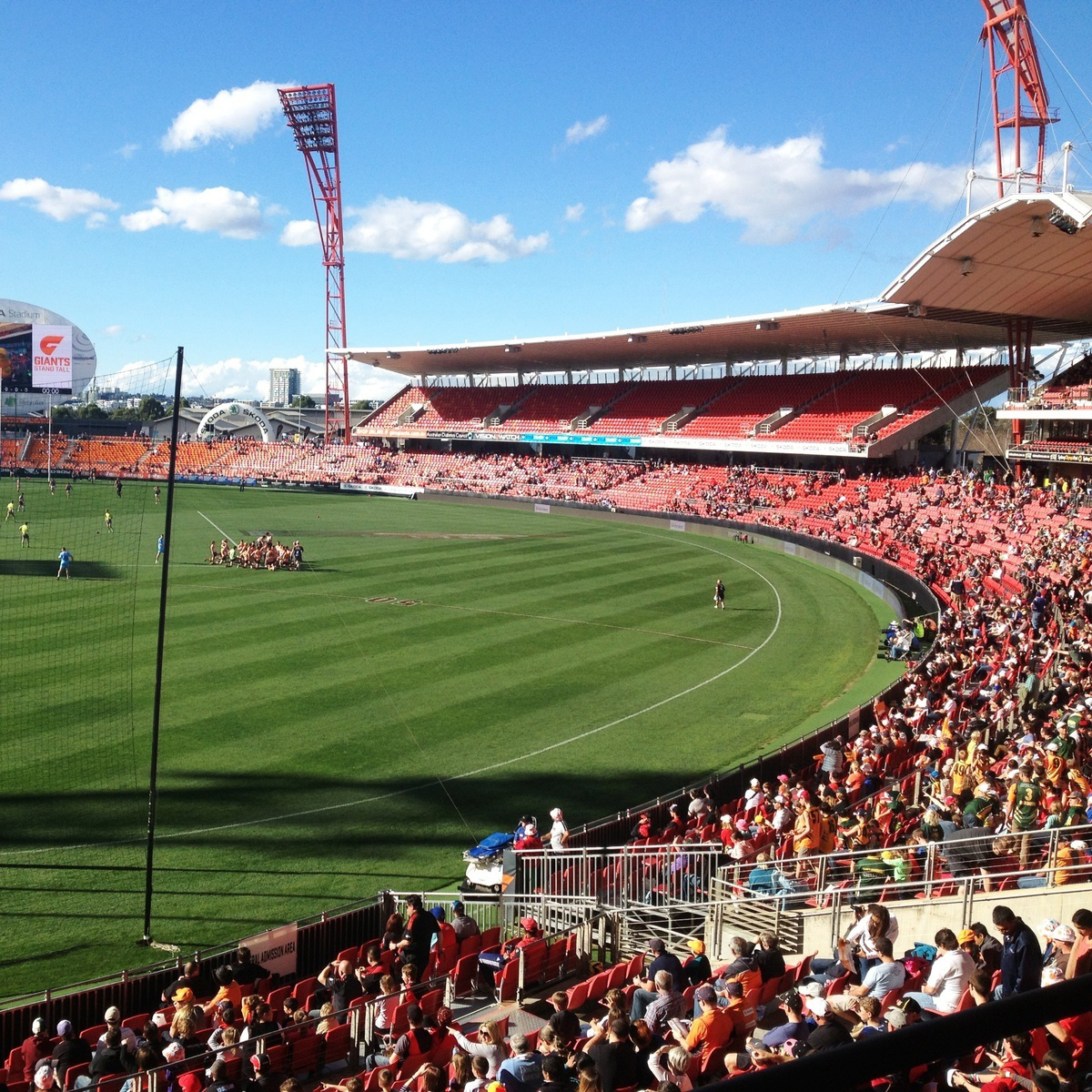 A view of ENGIE Stadium with players on the field and spectators filling red seats under a clear blue sky.